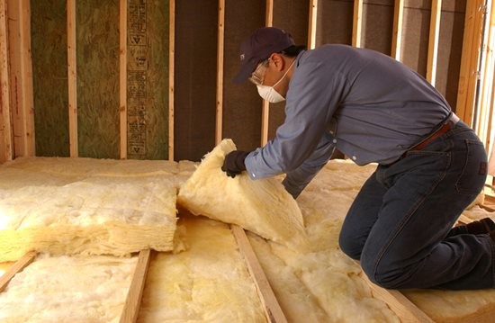 Technician installing yellow fiberglass batt insulation in an unfinished building