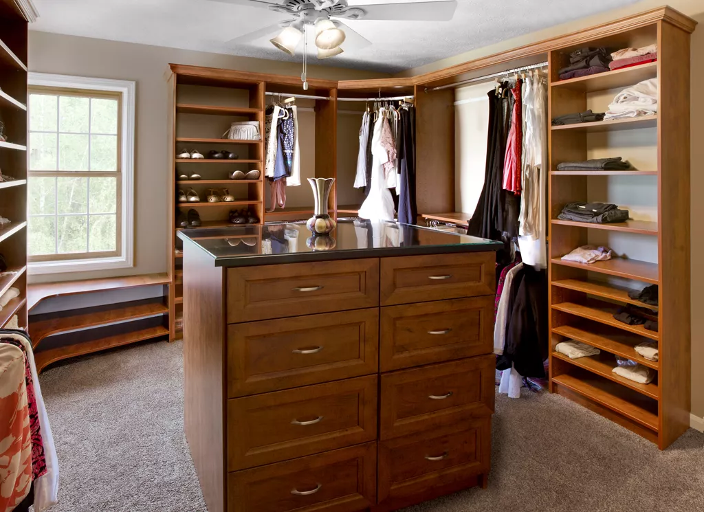 Enormous walk-in close with custom shelving, a corner bench under a window, tan carpet, and a ceiling fan.