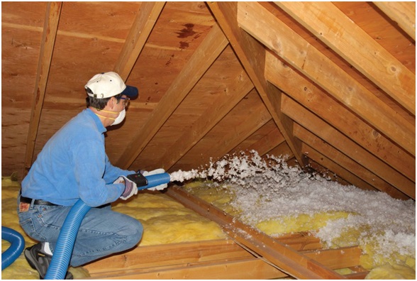 Technician blowing in loose-fill insulation in an unfinished attic.