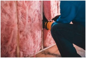 Insulation contractor installing pink fiberglass batt insulation in new construction